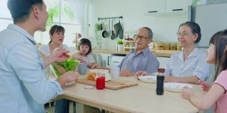 亚洲大家庭在家里的餐桌上一起吃午饭。年长的爷爷奶奶、年轻的夫妇和年幼的女儿感到高兴，在家里享受吃面包。活动关系的概念