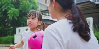 亚洲妈妈早上在街上骑自行车锻炼，给可爱的小女儿戴上运动头盔。快乐的少女戴上防护头盔，以保健康、保安全