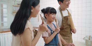 亚洲幸福的家庭呆在家里，在厨房，花时间一起烘焙，烘焙和食物。小孩子和父母在一起，爸爸妈妈唱歌跳舞，在家里享受亲子活动关系。