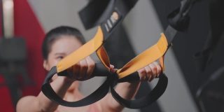 亚洲活跃的女运动员伸直双臂，握住一根固定在体育场钢梁上的绳子。女运动员在健身俱乐部或健身房进行上下举重运动，以保持肌肉，增强力量和灵活性