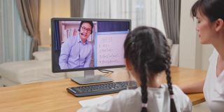 由于冠状病毒大流行，亚洲小女孩通过数字远程互联网会议向学校老师学习在线课程。孩子看着电脑，在妈妈的帮助下写纸条
