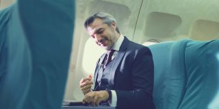 一位亚洲高管商人坐在商务头等舱，在飞机上用笔记本电脑工作。这名男子喜欢用手机听音乐，独自坐在飞机上感觉放松、快乐和快乐。