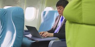 一位亚洲高管商人坐在商务舱，在飞机上用笔记本电脑工作。这个人很忙，眼睛感到很累。关注医疗保健和技术为商务人士的理念。