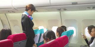 美丽的亚洲空姐或空中小姐在飞机起飞前走在过道上关闭行李舱并检查乘客。飞机客舱机组人员安全检查程序。