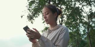 亚洲年轻活跃的女性站着，看着智能手机，与朋友和家人用手机交流，然后继续慢跑锻炼，在街道上公园跑步。
