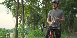 亚洲年轻活跃男性在骑完自行车后，休息一下，从瓶子里喝水，以保持健康。运动员在公园里骑自行车锻炼身体是为了自己的健康和健康。