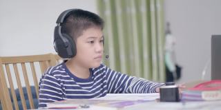新常态亚洲男孩学习在线看着屏幕笔记本电脑，在家里专心写作。技术教育的概念