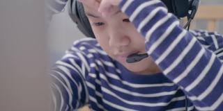 现代亚洲孩子上网学习，看着笔记本电脑屏幕，挠头，对学习问题感到头晕。技术教育理念在家工作