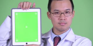 亚洲男医生的工作室肖像微笑和显示从数字平板电脑在绿色背景的复制空间