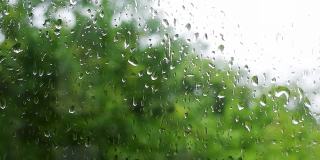 雨滴落在窗户上的4K原始视频，在绿树摇曳的散景背景下特写。