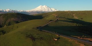 欧洲最高峰厄尔布鲁斯的鸟瞰图。俯瞰绿地、蜿蜒的道路和高加索山脉。埃尔布鲁士山的日出