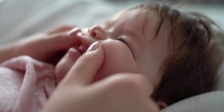 小白种人婴儿的脸部特写，她的妈妈用手按摩她的牙龈，以帮助她的牙齿生长，在家里的牙齿问题