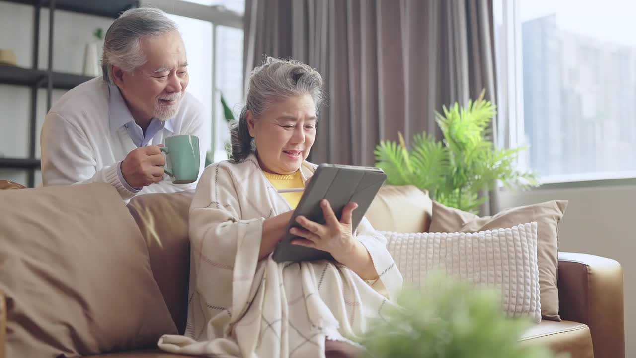 亚洲老年退休夫妇在沙发上与家人一起享受视频通话，幸福地笑着笑着，快乐地呆在家里，亚洲老年成熟成人居家隔离期概念
