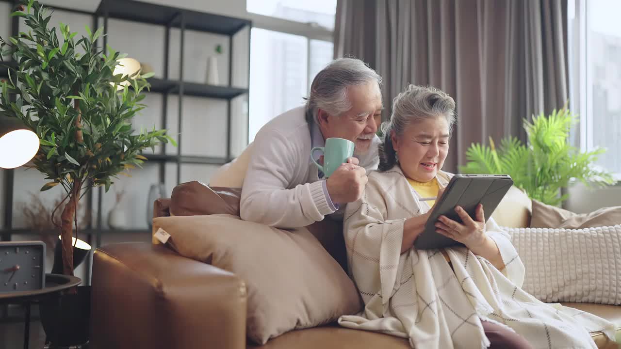 亚洲老年退休夫妇在沙发上与家人一起享受视频通话，幸福地笑着笑着，快乐地呆在家里，亚洲老年成熟成人居家隔离期概念