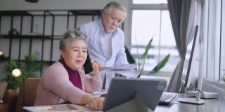 老的资深亚洲退休企业家在家里一起工作，在家隔离远程工作，用台式电脑和智能手机技术设备在家工作