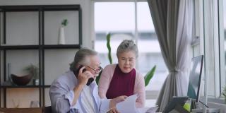 老的资深亚洲退休企业家在家里一起工作，在家隔离远程工作，用台式电脑和智能手机技术设备在家工作