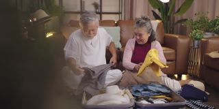 年迈的亚洲老人夫妇一起收拾行装，幸福的亚洲老年退休的成年人享受在家里客厅室内背景地板上一起整理布