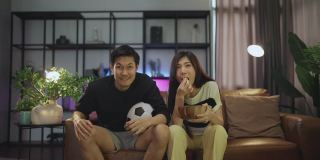 结婚成人亚洲人在家里看电视，亚洲夫妇一起欢呼体育比赛比赛笑胜利在沙发沙发上在客厅家隔离活动