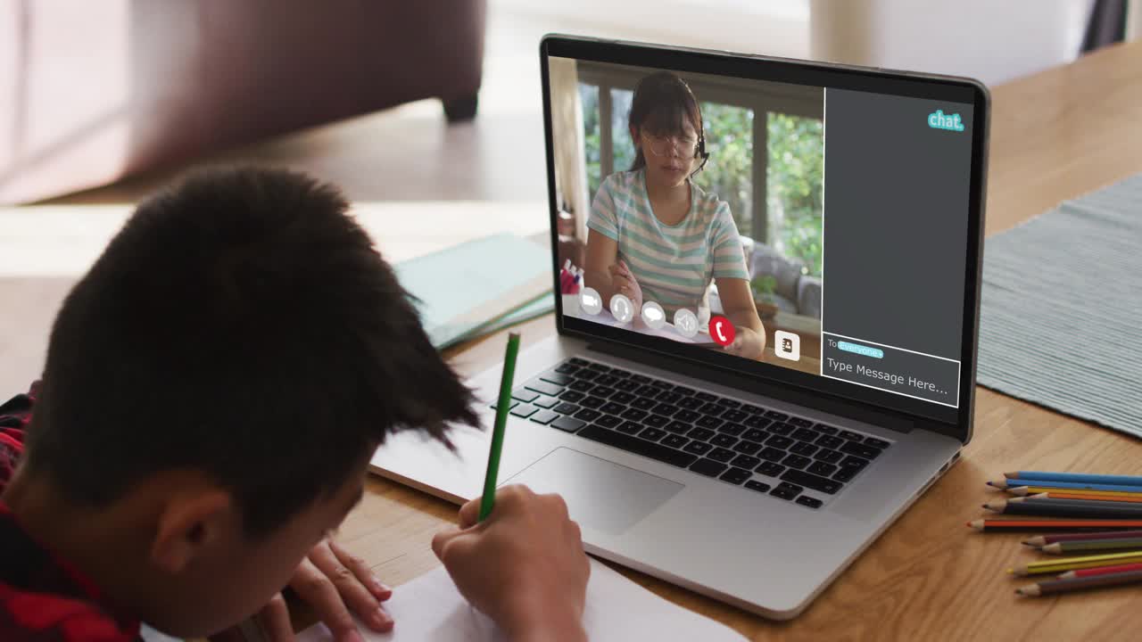 亚洲男孩在家里用笔记本电脑做作业，和女老师视频通话