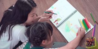 妈妈正在帮她的女儿做家庭作业和在书上涂色。艺术教育和创意活动地板。