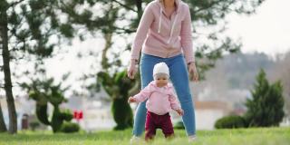 一位白人母亲教婴儿走路。母亲和孩子在公园里散步。真正的时间。缓慢的运动。儿童发展的概念