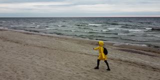一个穿着黄色外套，背着麻袋的女人在寒风中走在海边