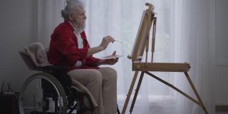 集中才华横溢的残疾人坐在轮椅上眺望窗外。侧面视野宽的启发白人残疾退休享受爱好在家里室内。缓慢的运动。