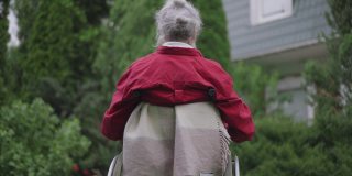 后视图白发残障老人在轮椅上伸展在夏天的后院花园的户外。伤残退休人员享受闲暇的中景。缓慢的运动。