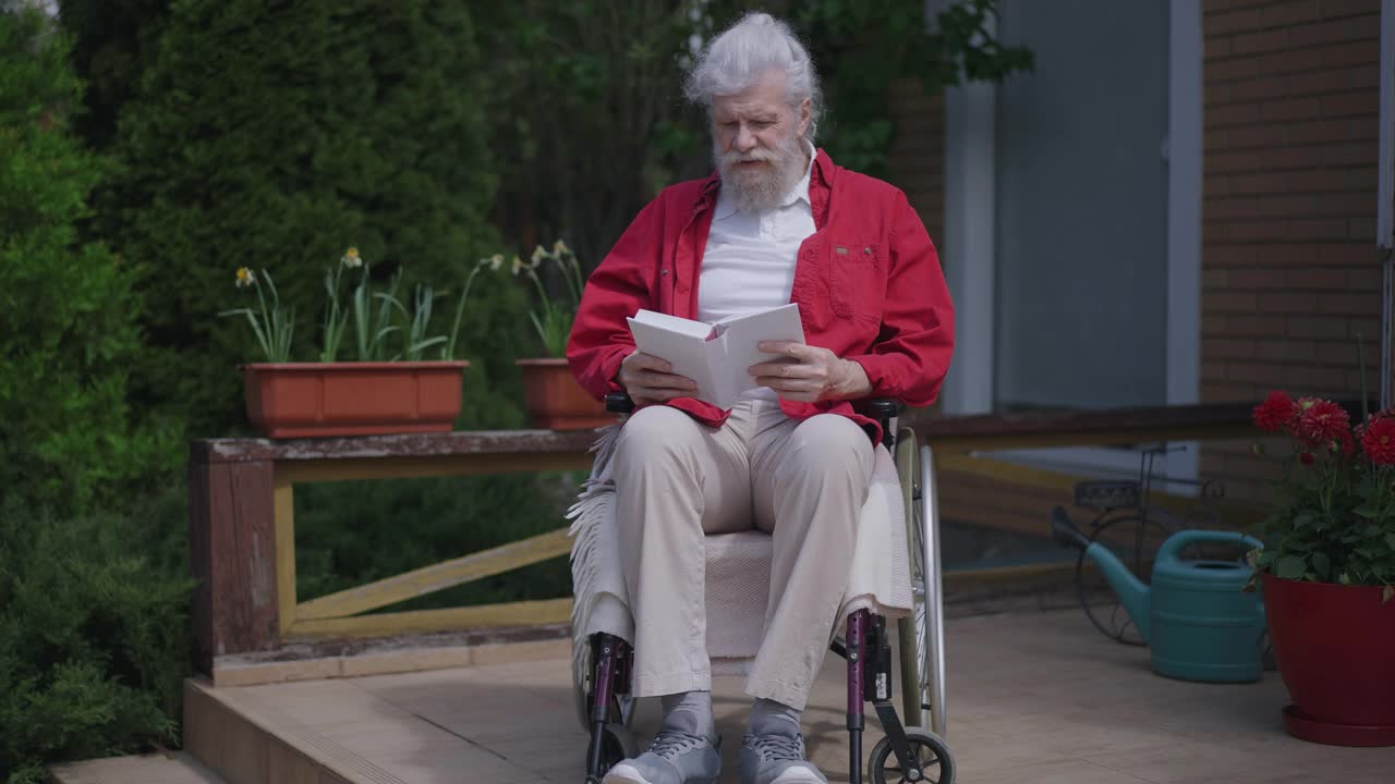 老年残障智人在阳光明媚的户外，坐在轮椅上看书。享受嗜好的白种人受损退休人员的广角正面照片。生活方式和残疾。