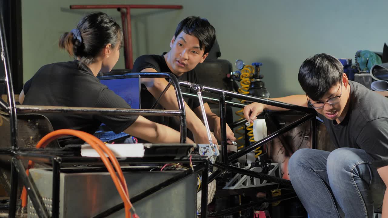 三个十几岁的亚洲学生团队合作开发在项目工程课上通过笔记本电脑控制在学校的一个研究实验室工作到深夜。有创意的设计师测试机器人。技术、团队合作的概念