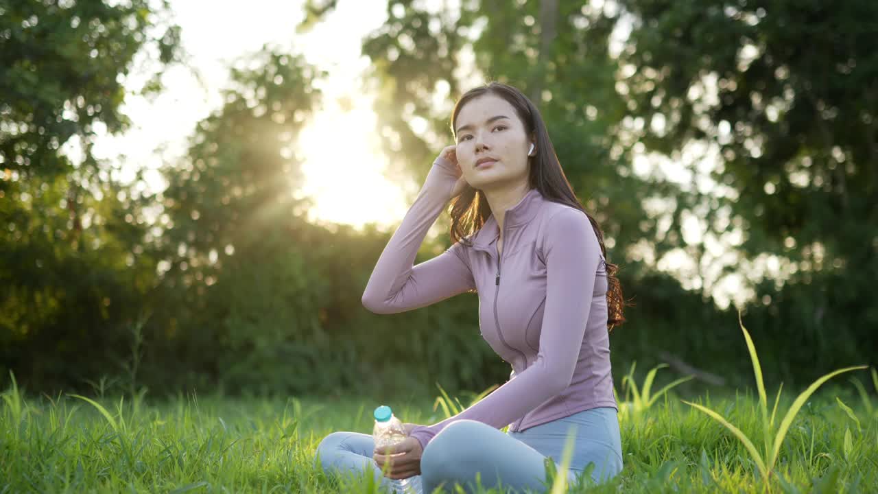 穿着运动服的亚洲女人坐在瑜伽垫上喝水