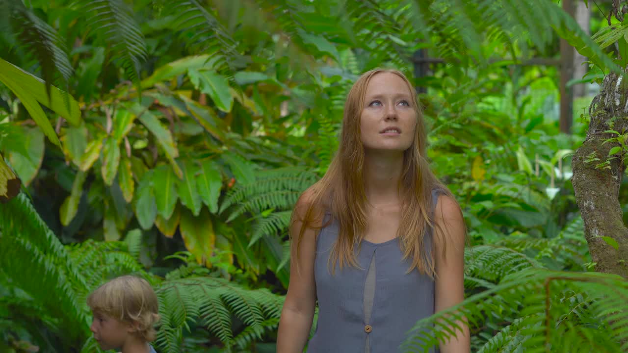 一位年轻的妇女和她的儿子参观一个热带植物园。蕨类植物区