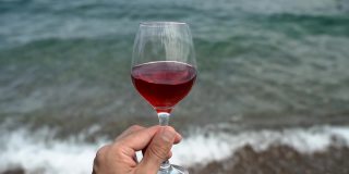 在地中海和海滩的背景下，手里拿着葡萄酒。品鉴红酒，享受美酒的美与味