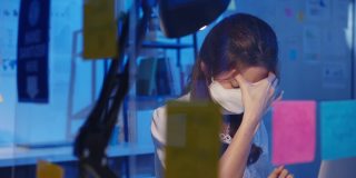 紧张疲惫的亚洲年轻女性戴着口罩使用笔记本电脑努力工作患有办公室综合症，颈部疼痛，同时在办公室加班。