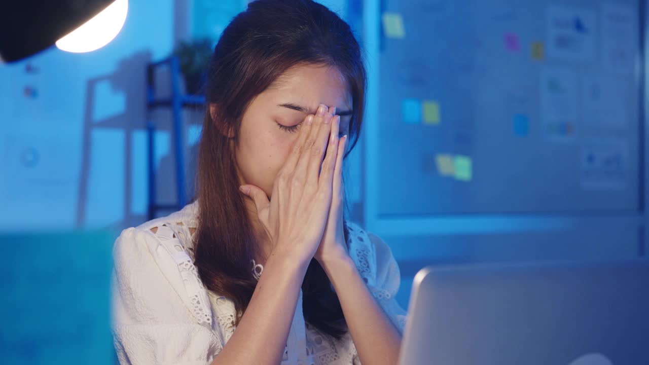 紧张疲惫的年轻亚洲女士使用笔记本电脑辛勤工作患有办公室综合症，在办公室加班时脖子疼。