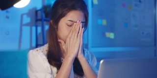 紧张疲惫的年轻亚洲女士使用笔记本电脑辛勤工作患有办公室综合症，在办公室加班时脖子疼。