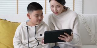 Portrait亚洲家庭妈妈和儿子孩子在家里学习在平板电脑上。