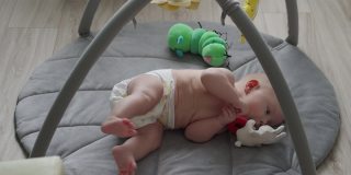 可爱的3个月的小男孩学习从他的背部到腹部，当他躺在游戏垫上，婴儿活动在婴儿游乐场的软垫上。