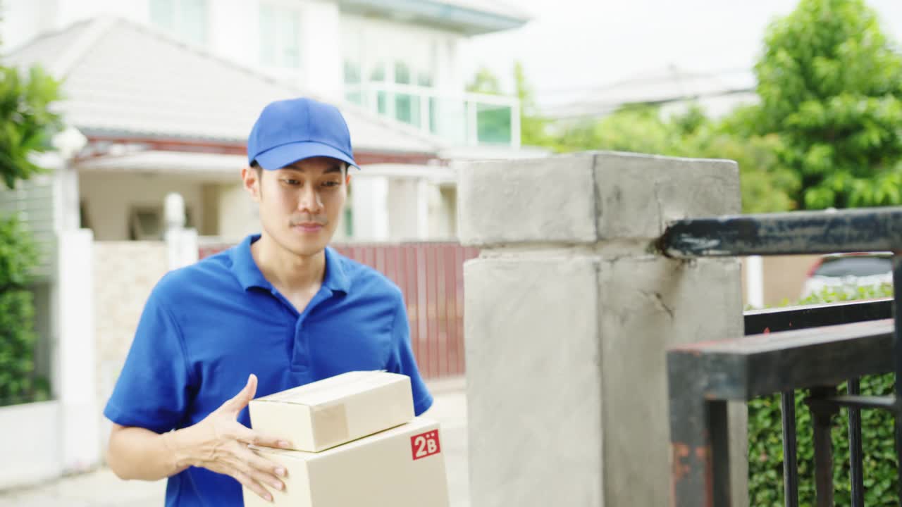 年轻的亚洲邮政快递员穿着蓝色衬衫处理包裹盒寄给客户在家里和亚洲女性收到包裹在户外。