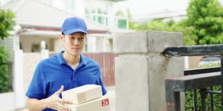 年轻的亚洲邮政快递员穿着蓝色衬衫处理包裹盒寄给客户在家里和亚洲女性收到包裹在户外。
