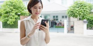 有魅力的年轻亚洲女商人使用手机查看社交媒体互联网，在城市的街道上与朋友聊天。