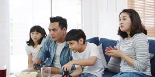 快乐亚洲家庭爸爸，妈妈和孩子有趣的玩电子游戏与技术控制台在家里的客厅。