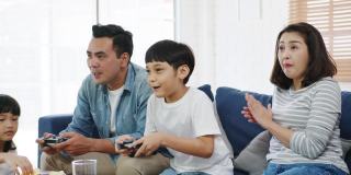 快乐亚洲家庭爸爸，妈妈和孩子有趣的玩电子游戏与技术控制台在家里的客厅。