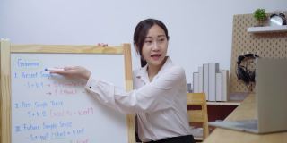 亚洲女教师在白板上写字，在家使用笔记本电脑进行在线教学