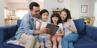 快乐快乐的亚洲家庭爸爸，妈妈和孩子在家里的沙发上玩数码平板视频通话。