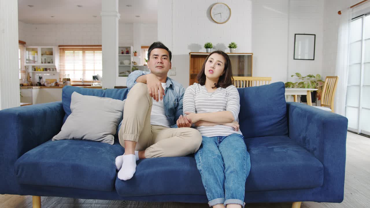 亚洲家庭爸爸和妈妈坐在沙发上感到烦恼和疲惫，而女儿和儿子在家里客厅的沙发上玩耍大喊大叫。