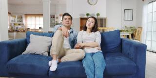 亚洲家庭爸爸和妈妈坐在沙发上感到烦恼和疲惫，而女儿和儿子在家里客厅的沙发上玩耍大喊大叫。