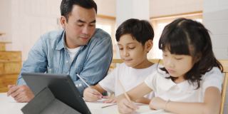 快乐亚洲家庭家庭教育，爸爸在家里的客厅教孩子使用数码平板电脑。