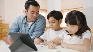 快乐亚洲家庭家庭教育，爸爸在家里的客厅教孩子使用数码平板电脑。视频素材模板下载