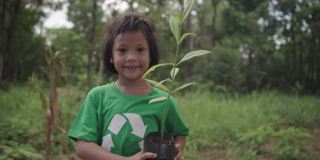 可爱的女孩站着，拿着一棵植物，她准备在森林里种一棵树。